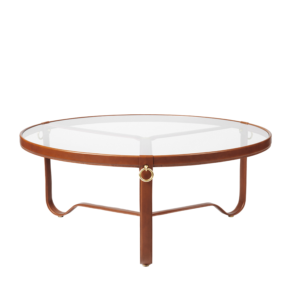 The Adnet is a coffee table set on three curved metal legs. The circular glass top is framed by a hand-finished leather rim and detailed with signature gilded brass rings. 